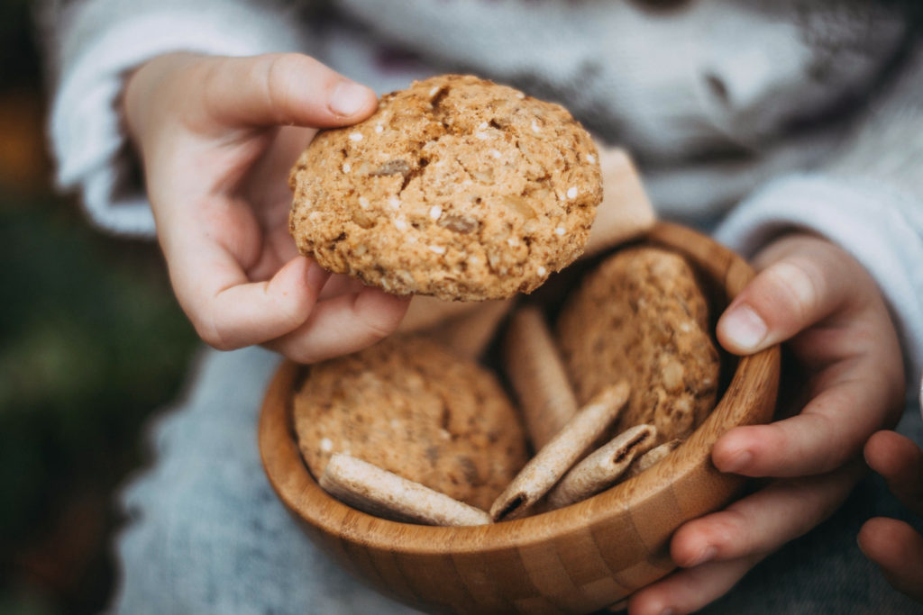 person holding a wooden bowl of rustic oatmeal cookies