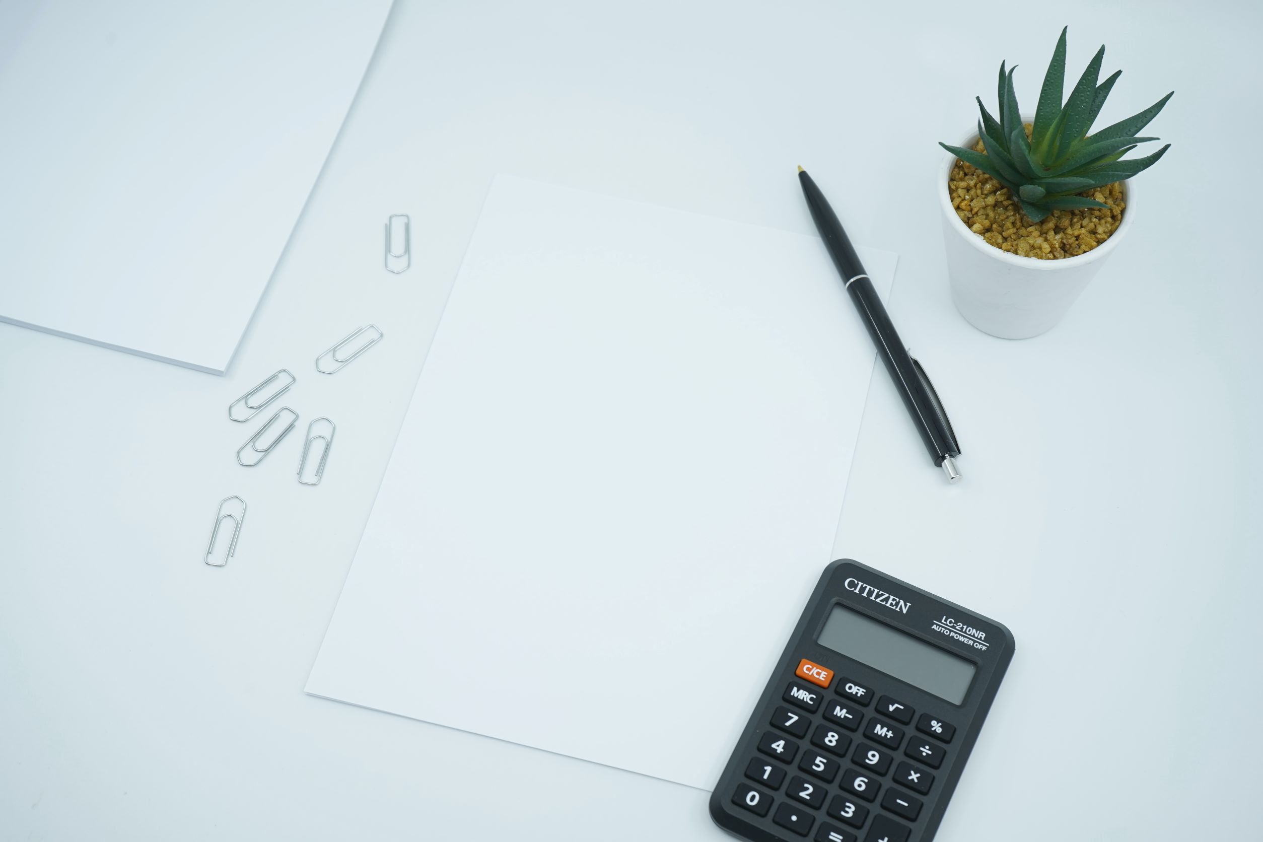 calculator and pen sitting on desk next to potted plant
